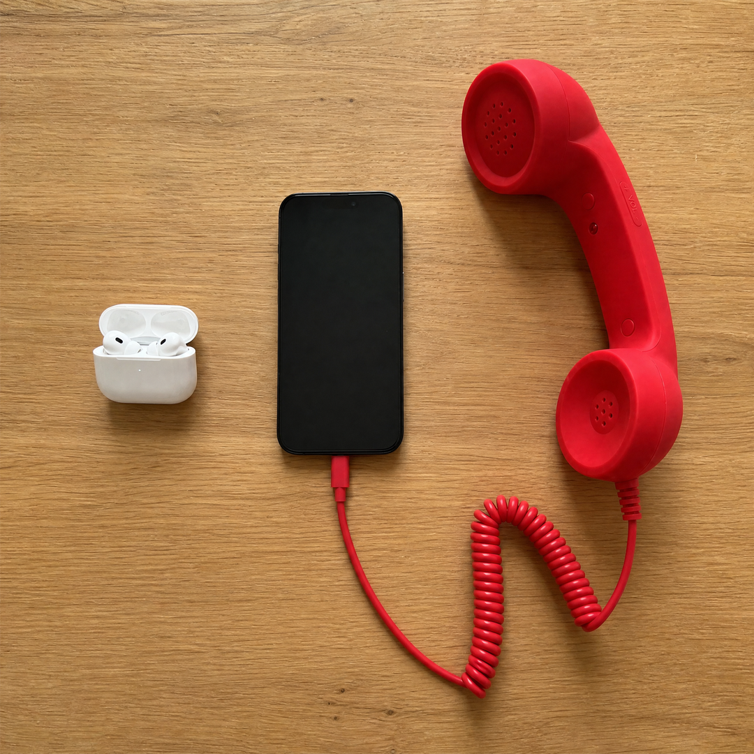 Overhead: a wireless earbuds case, a phone, and the red DialBop handset plugged into it, laid out on an oak table
