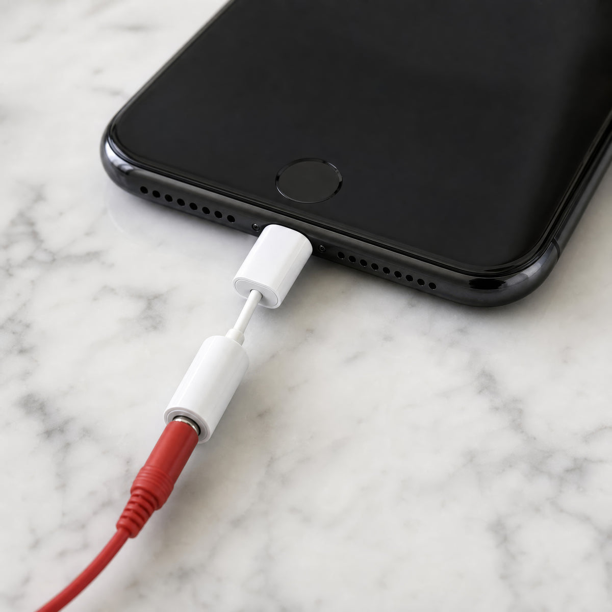 Lightning option: the white Lightning to 3.5 mm adapter in an iPhone on a marble counter, the red DialBop jack seated in its socket