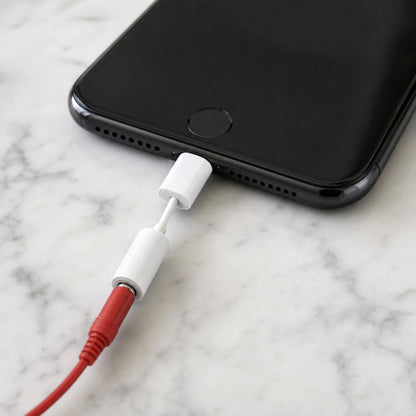Lightning option: the white Lightning to 3.5 mm adapter in an iPhone on a marble counter, the red DialBop jack seated in its socket