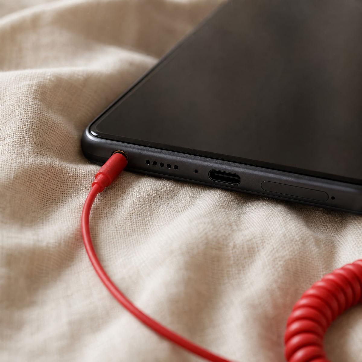 The red 3.5 mm jack on the DialBop cord in the headphone socket of a phone on a linen sheet