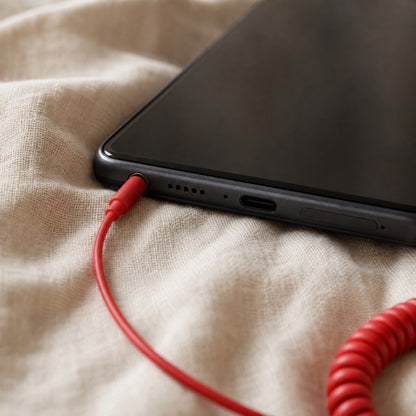 The red 3.5 mm jack on the DialBop cord in the headphone socket of a phone on a linen sheet